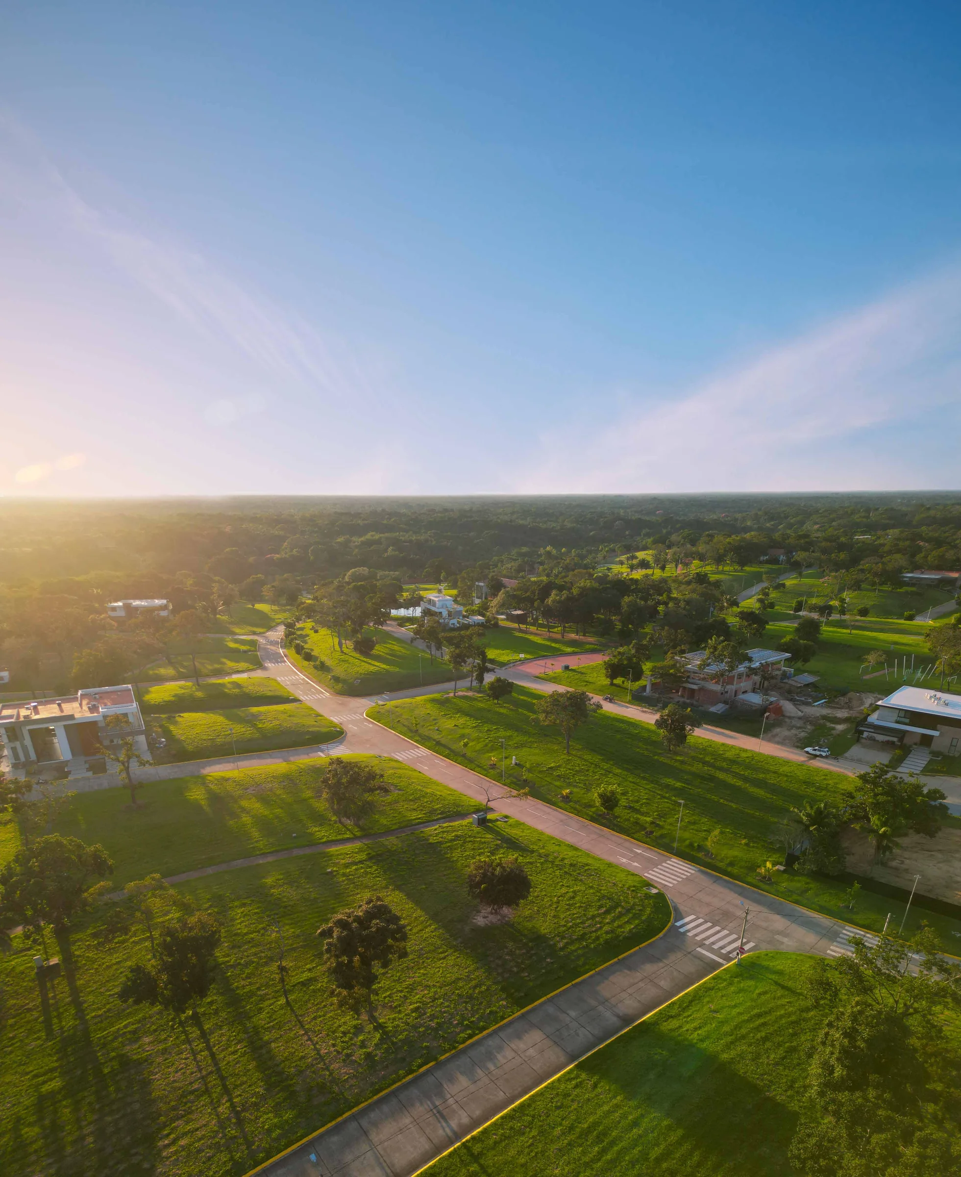 Vista aérea de las calles, áreas verdes y viviendas de Urubó Village al atardecer